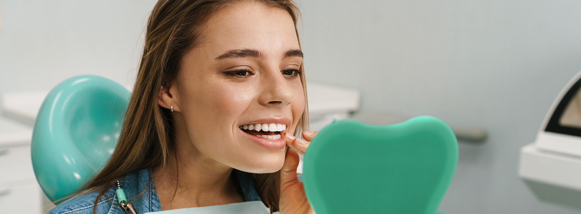 A young woman is seen smiling at the camera, holding a green object that appears to be a toothbrush with a blue handle.