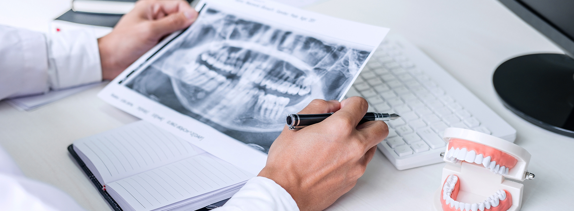 A dental professional examining a model of a human mouth with a pen in hand, surrounded by medical equipment and documentation.