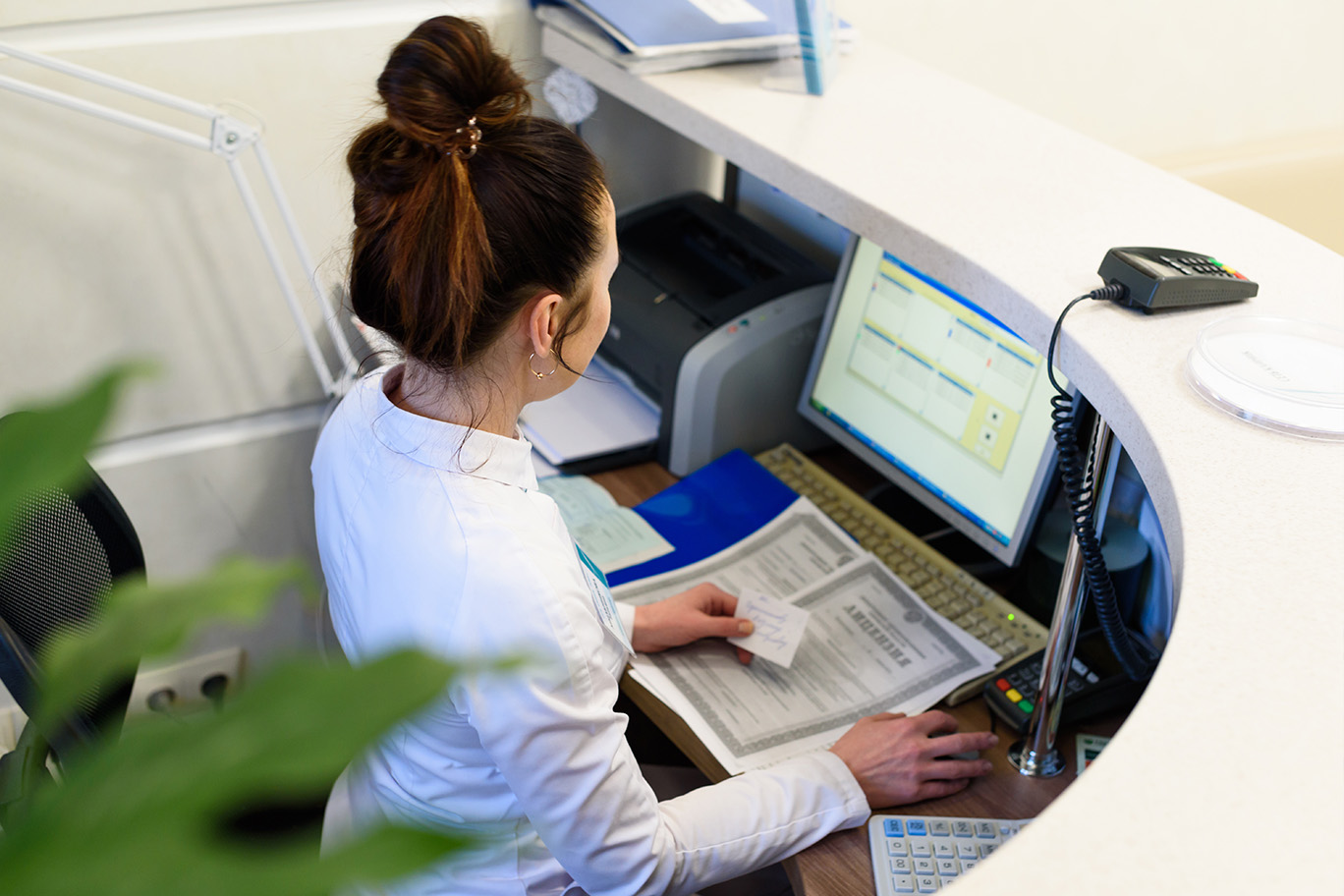 Woman working at a counter with a computer and various documents.