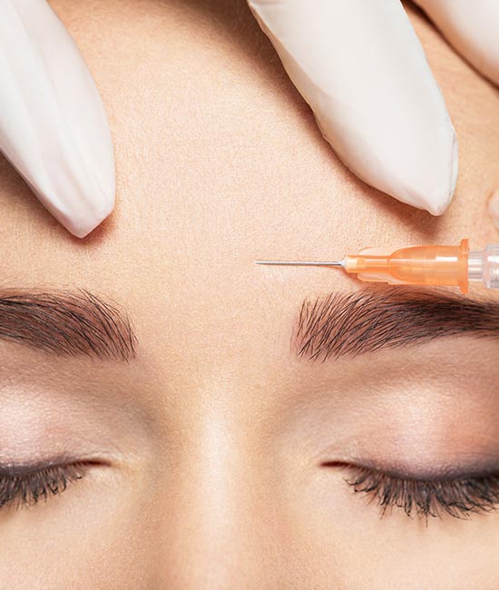 This is a photograph of a person undergoing a cosmetic procedure, with a syringe inserted into their skin above the eyebrow. The individual has closed eyes and appears to be resting or relaxing during the process.
