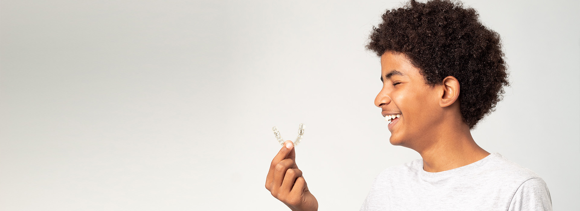 A young individual holding a small white object, smiling and looking directly at the camera.