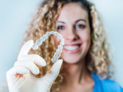A woman is holding a large, clear dental retainer with her right hand.