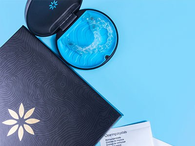 An image of a dental implant kit with an open case containing a blue item, possibly a tool or instrument, placed on a blue background next to a closed box with a white lid and a black label.