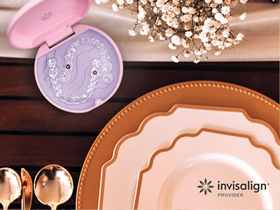 The image is a promotional advertisement for Invisalign, featuring a table setting with plates and a box of dental aligners.