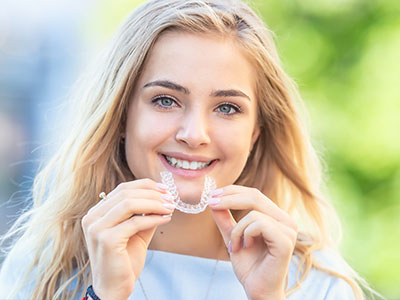 The image features a smiling woman holding a toothbrush with bristles and toothpaste, showcasing the product while standing outdoors.