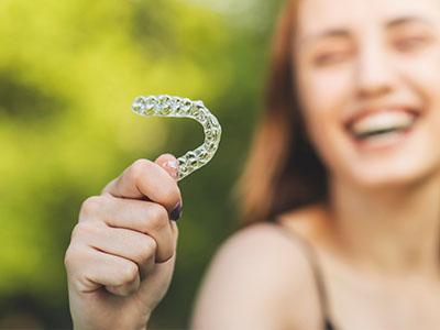 A smiling woman holds a transparent, plastic dental retainer in her hand.