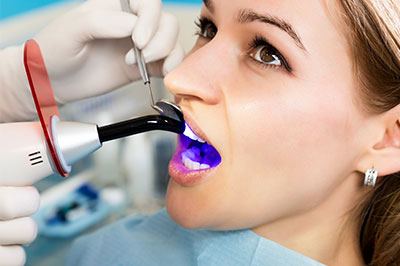 A woman receiving dental treatment, with a dentist using a specialized device to clean her teeth.