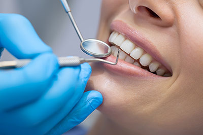 A dental hygienist performing teeth cleaning on a patient while wearing protective gloves and equipment.