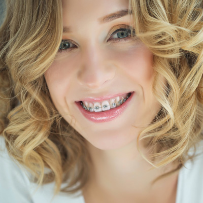 A woman with straight white teeth and a bright smile, wearing braces, poses for a portrait.