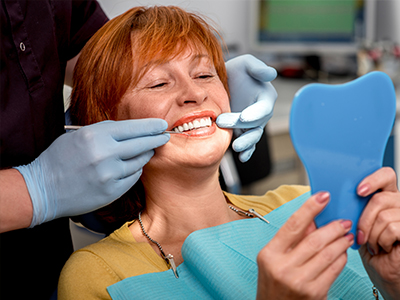 A woman receiving dental care, with a dental hygienist adjusting her mouthpiece and holding up a toothbrush.