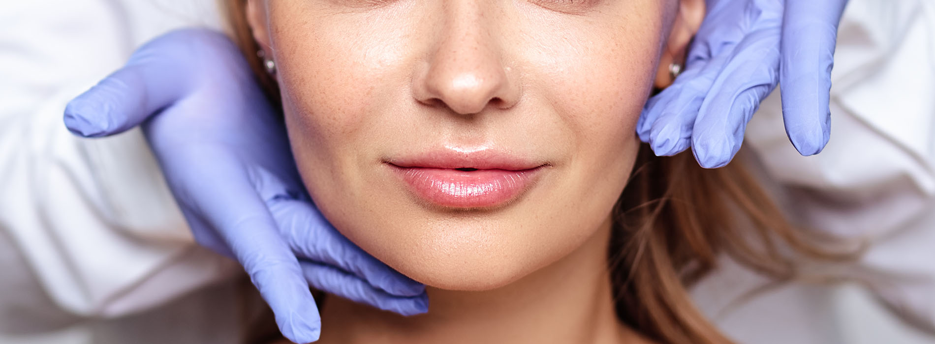 Woman receiving facial treatment with a medical mask and blue gloves.