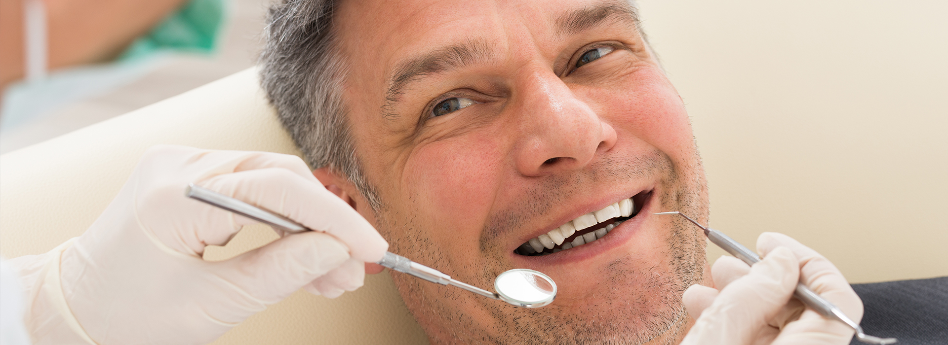 The image shows a man in a dental chair, smiling and looking at the camera, with dental tools visible around him.