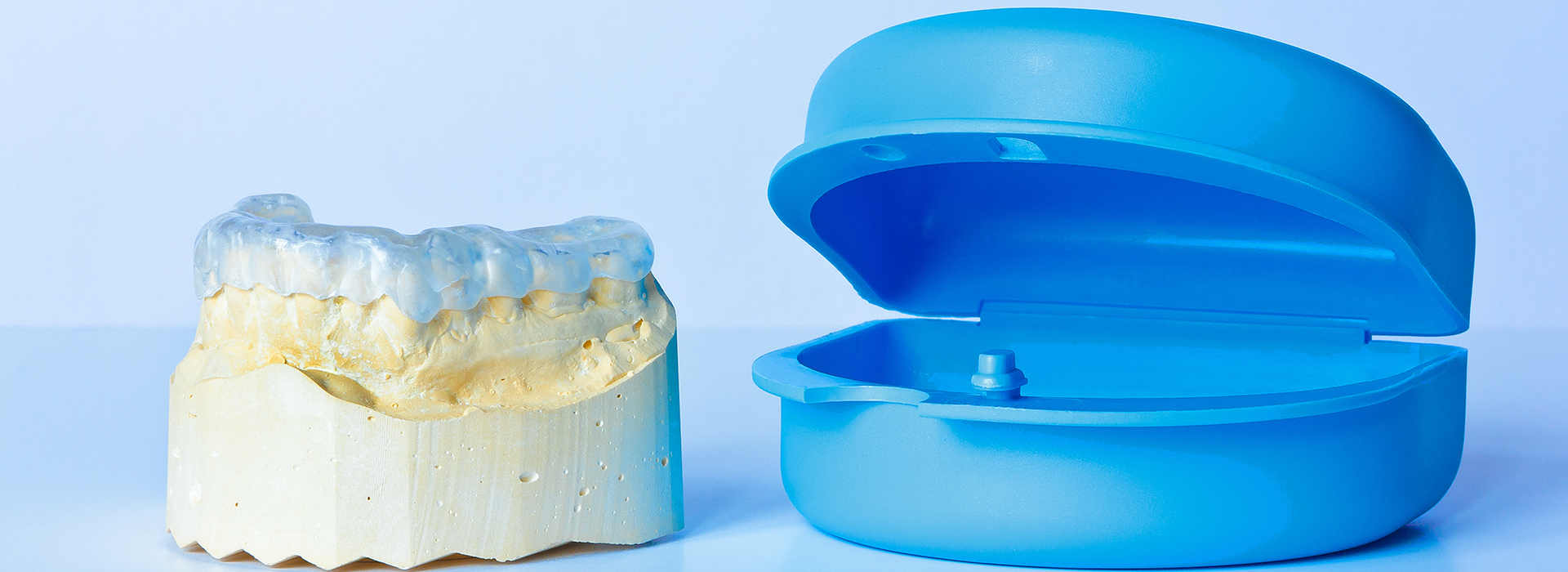 The image features a blue plastic model of a human tooth and its corresponding crown, placed side by side against a light background.