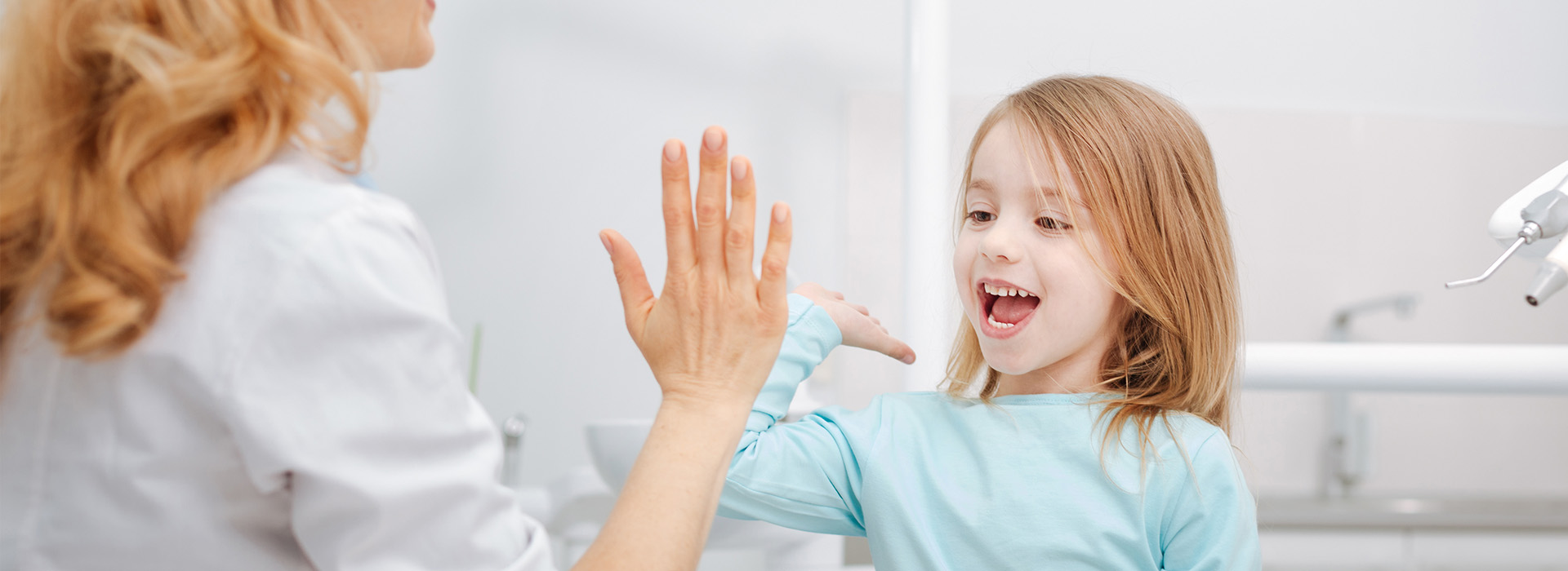 A woman and a young girl in a dental office, with the woman interacting with the child.