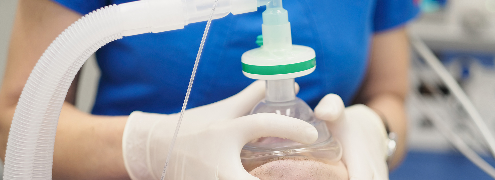 The image shows a person wearing gloves and a mask, holding a syringe with a clear liquid in it.