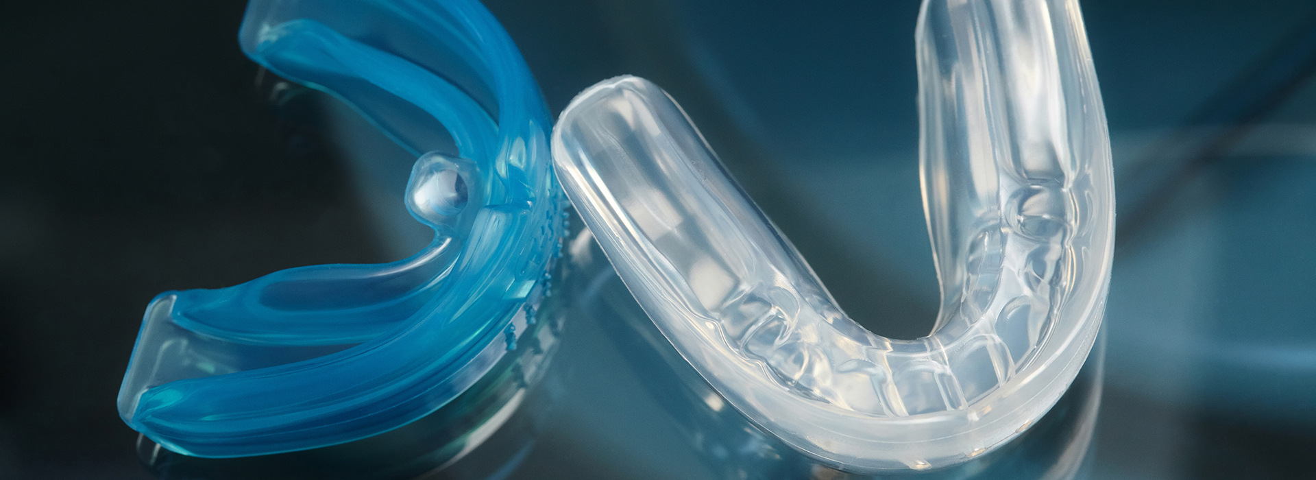 The image shows a clear plastic object with a blue tint, resembling a dental retainer or orthodontic appliance, placed against a blurred background.