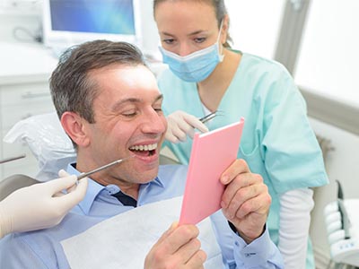 The image shows a man holding up a pink card with a surprised expression, surrounded by dental professionals who appear to be in a dental office setting.