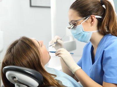 A dental hygienist assisting a patient during a teeth cleaning appointment, with both individuals wearing masks and gloves.