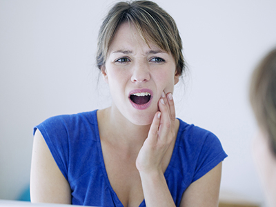 A woman with a concerned expression, touching her face and mouth area.