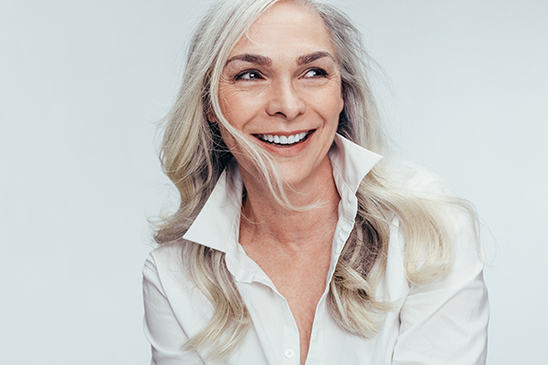 The image shows a woman with blonde hair, wearing a white top and smiling at the camera.