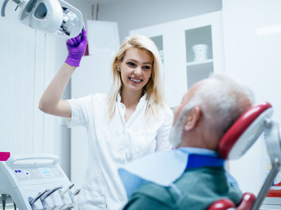 The image shows a dental professional, likely a dentist, assisting an older patient during a dental procedure.