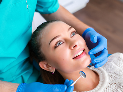 A dental hygienist is performing a teeth cleaning procedure on a woman in a dental office.