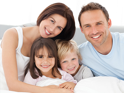 A family of four, including a man, woman, and two children, posing together on a bed.