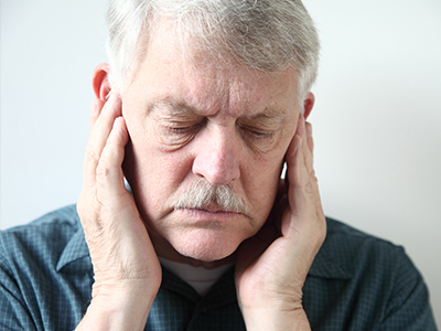 The image features an elderly man with a mustache, wearing glasses and holding his face with both hands, seemingly in pain or discomfort.