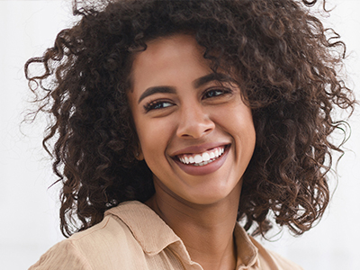 A smiling woman with curly hair, wearing a light-colored top.